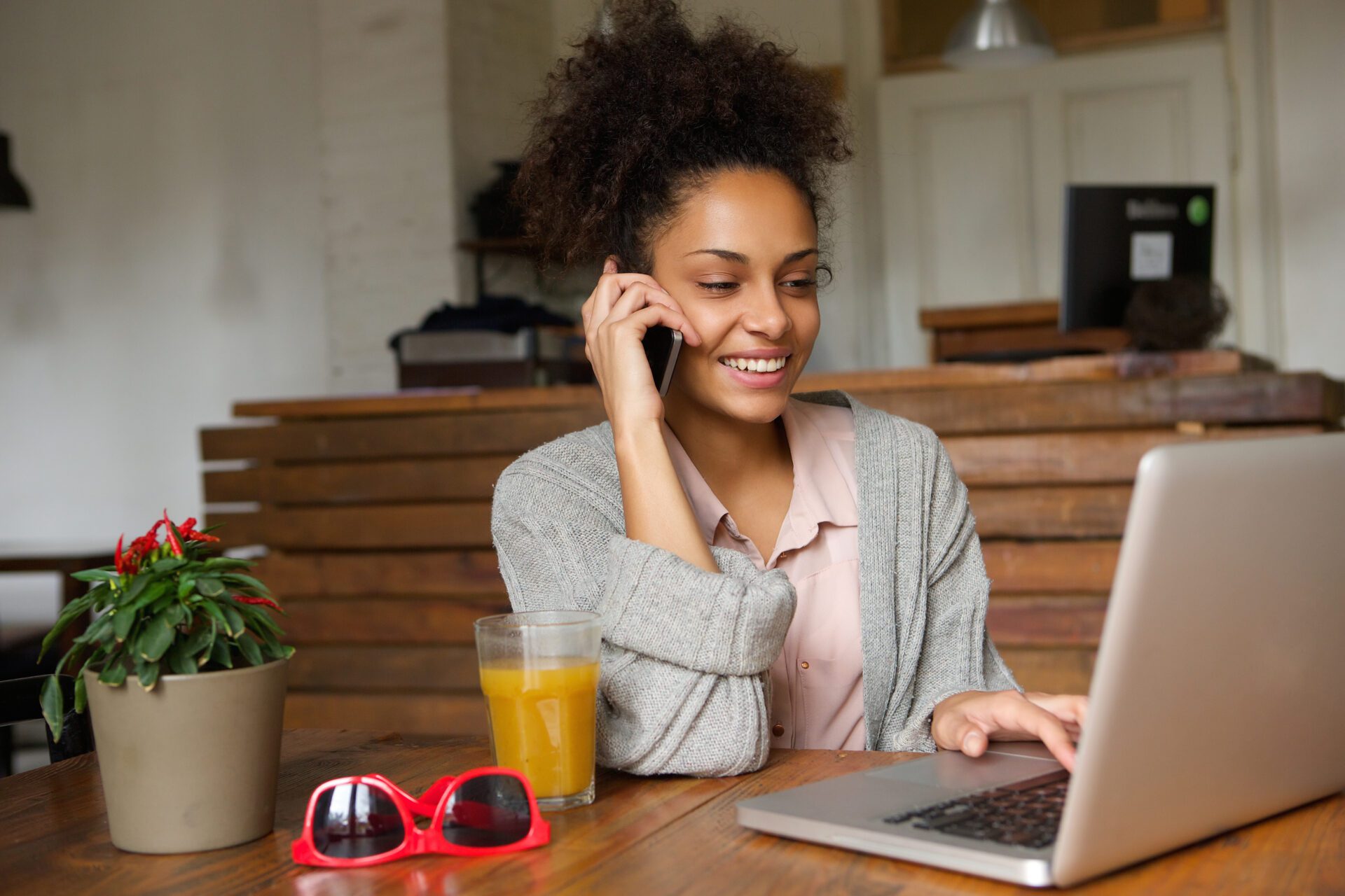 Portrait of a smiling young woman using laptop and talking on mobile phone